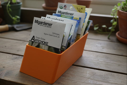 Orange container holding seed packets on a potting bench
